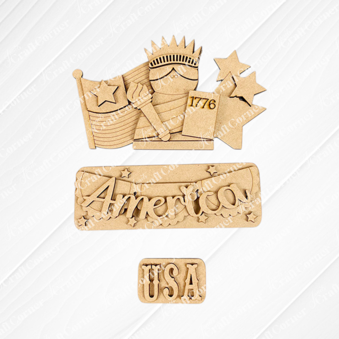 Wooden cutouts on a textured background celebrate Americana, showcasing the Statue of Liberty, an American flag with stars, a "1776" sign, the word "America" adorned with stars, and "USA" below. Perfect for Janet's Craft Corner's America Interchangeable Insert DIY home decor kit.
