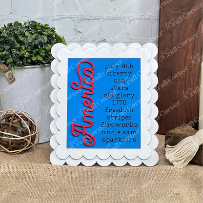 Janet's Craft Corner Patriotic Farmhouse Signs DIY kit features a scalloped white frame and “America” in red script on blue, plus patriotic words—perfect seasonal tiered tray decor or to pair with a potted plant. Set of 1.