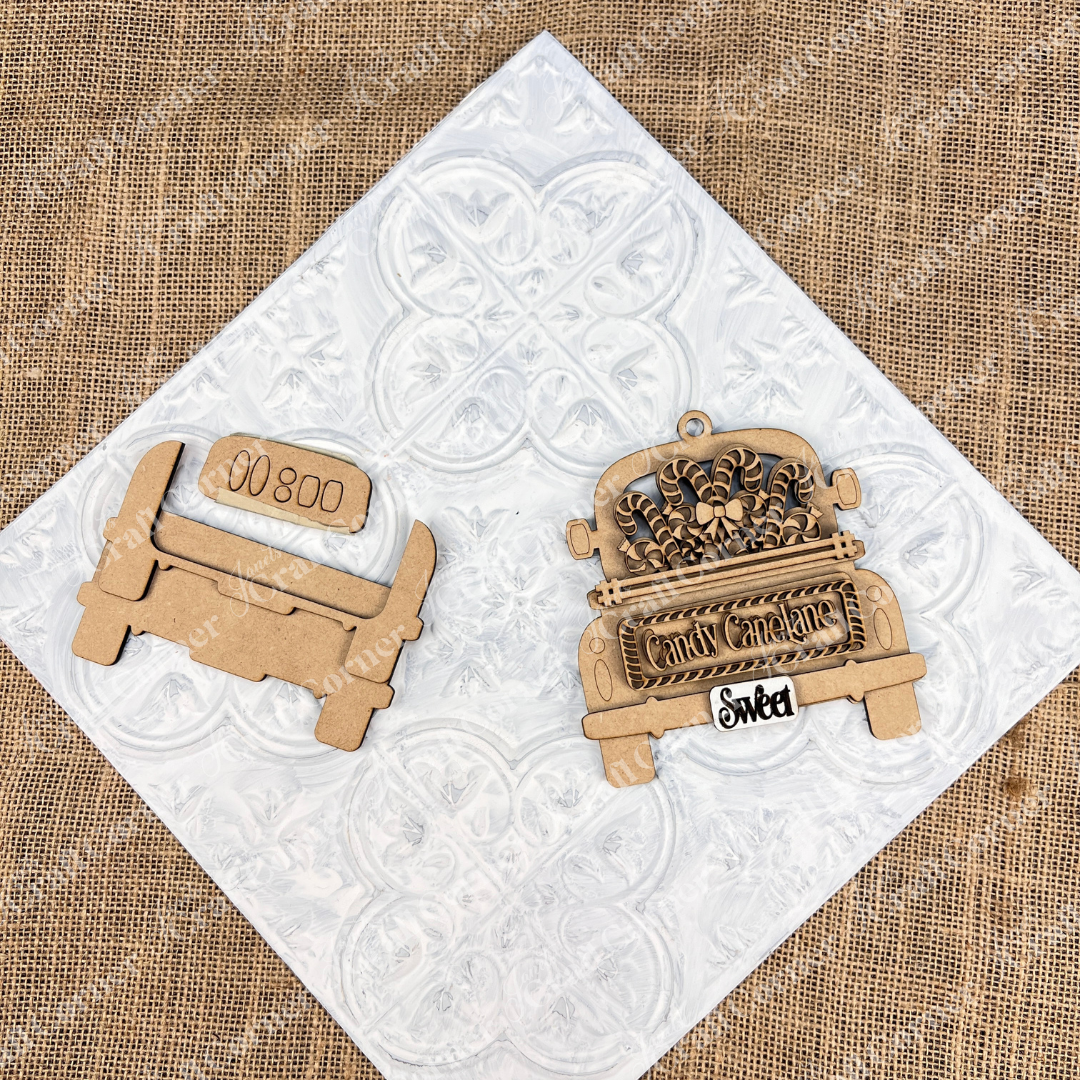 A wooden Christmas ornament rest elegantly on a textured white and burlap background. The Antique Truck Ornament from Janet's Craft Corner features the delightful phrases "Candy Cane Lane" and "Sweet"  This piece is perfect as Christmas décor or as part of a DIY Decoration Kit for crafting enthusiasts.