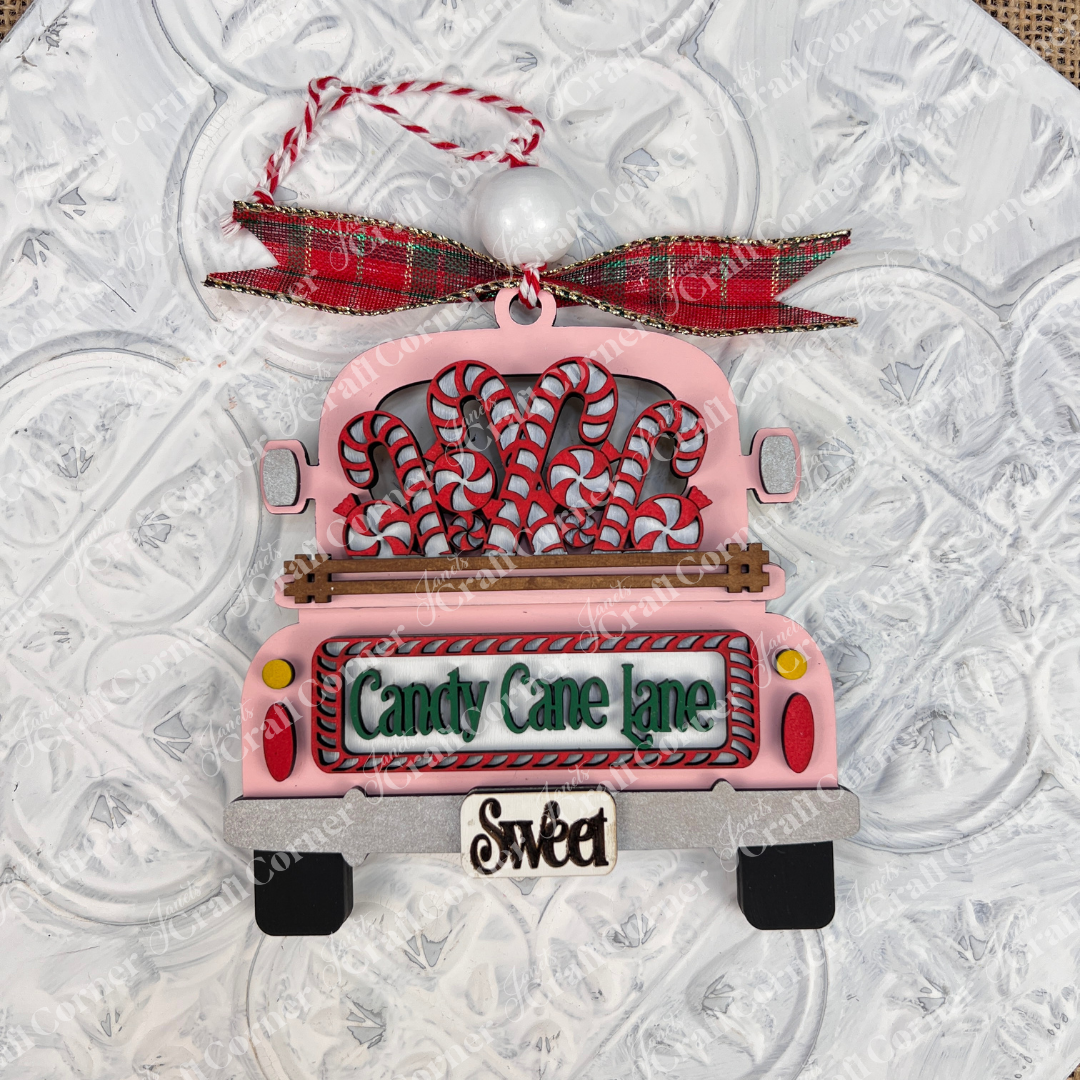 Add a delightful touch to your holiday season with Janet's Craft Corner's Antique Truck Ornament, an exquisite DIY decoration kit. This charming Christmas piece features a pink antique truck adorned with candy canes and topped with a red plaid bow. The back reads "Candy Cane Lane" and "Sweet," all set against a textured white background.
