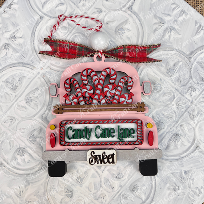 Add a delightful touch to your holiday season with Janet's Craft Corner's Antique Truck Ornament, an exquisite DIY decoration kit. This charming Christmas piece features a pink antique truck adorned with candy canes and topped with a red plaid bow. The back reads "Candy Cane Lane" and "Sweet," all set against a textured white background.