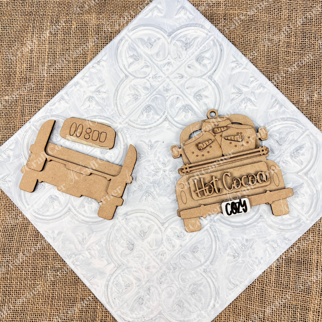 Create a delightful DIY kit with wooden cutouts from Janet's Craft Corner's "Antique Truck Ornament" collection. The truck features "Hot Cocoa" accompanied by mugs on the bed ideal for personalizing your Christmas décor. The pieces maintain their natural wood finish, highlighting their vintage charm against a textured background.