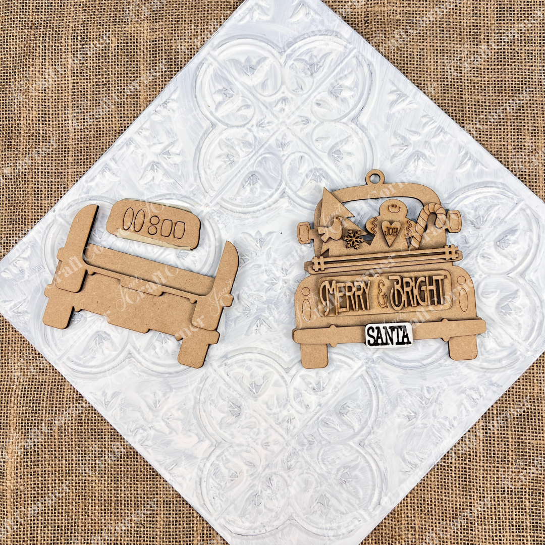 A wooden cutout kit from Janet's Craft Corner adds charm to a burlap and white patterned background.  It features an antique truck ornament design with the words "Merry & Bright" and "Santa," accompanied by a tree, snowman, and candy cane. This kit is perfect for your DIY Christmas décor project.
