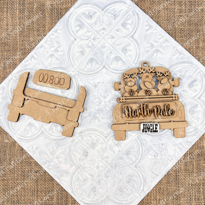 Displayed on a textured white and burlap background is a wooden cutout of a vintage truck. An Antique Truck Ornament from Janet's Craft Corner displays "North Pole," adorned with reindeer and a "Jingle" license plate. A perfect addition to your DIY decoration kits or Christmas décor collection.