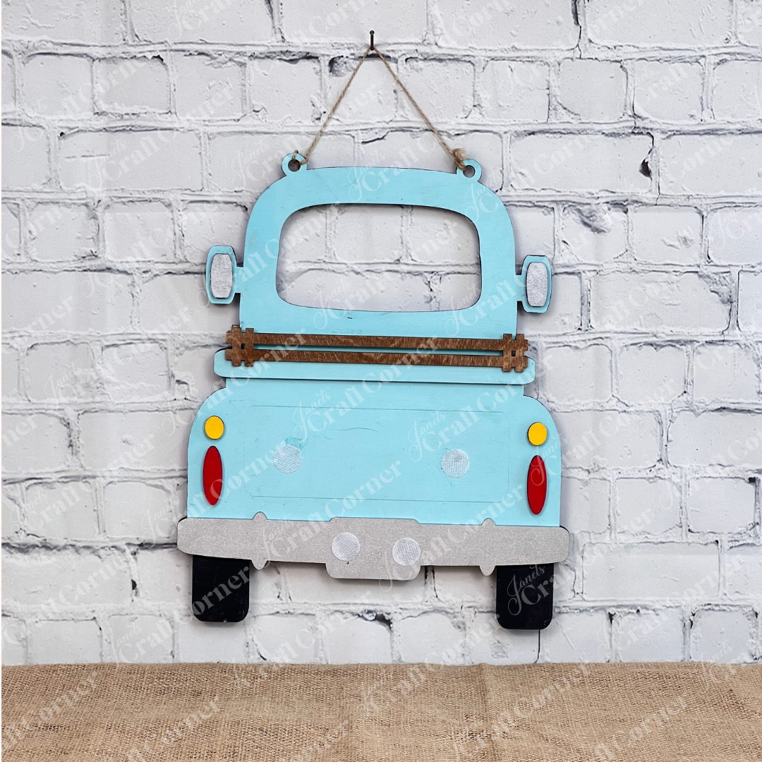 The Antique Truck Interchangeable Base  Hanging DIY home decor kit by Janet's Craft Corner features wooden cutout pieces which have been painted teal, displayed on a white brick background.