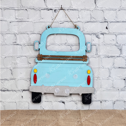 The Antique Truck Interchangeable Base  Hanging DIY home decor kit by Janet's Craft Corner features wooden cutout pieces which have been painted teal, displayed on a white brick background.