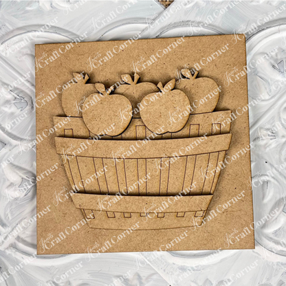 Janet's Craft Corner Apple Basket Square features a square wood piece with a raised, laser-cut basket of five apple cut-outs on a textured, painted white background—ideal unfinished DIY home decor.