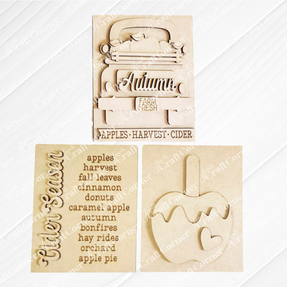 Displayed against a white plank wall this set of Apple Cider Switchable Farmhouse Signs are DIY seasonal home decor kits with a fall apple theme. One features the wood cut-out word “Cider Season” with words that evoke the scent of apples in the air, another features a caramel apple complete with heart and the last features an antique truck with a load of apples.