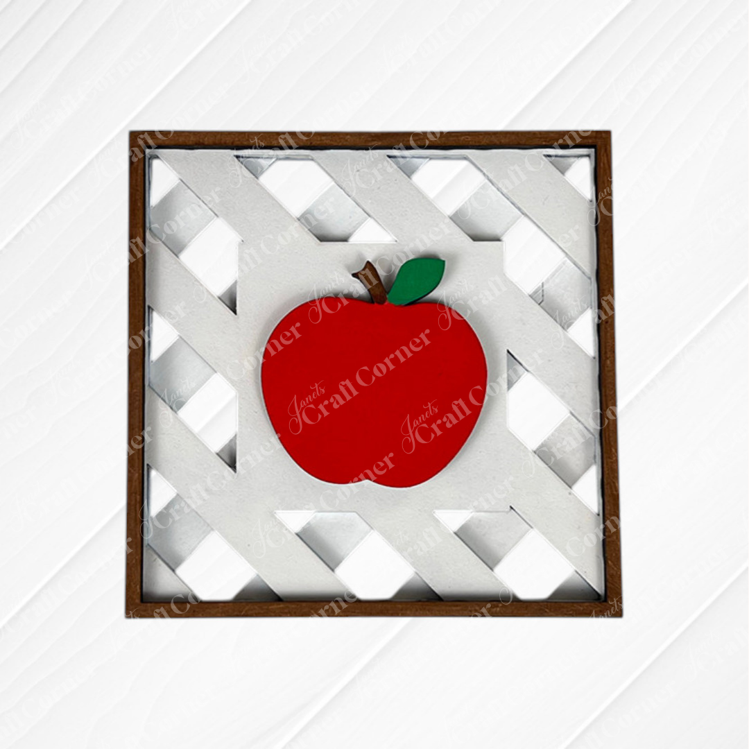 Janet's Craft Corner Apple on Lattice Square: Framed artwork with a bright red apple, green leaf, and brown stem on a white lattice background in a wooden border—ideal for DIY home decor or seasonal craft kits.