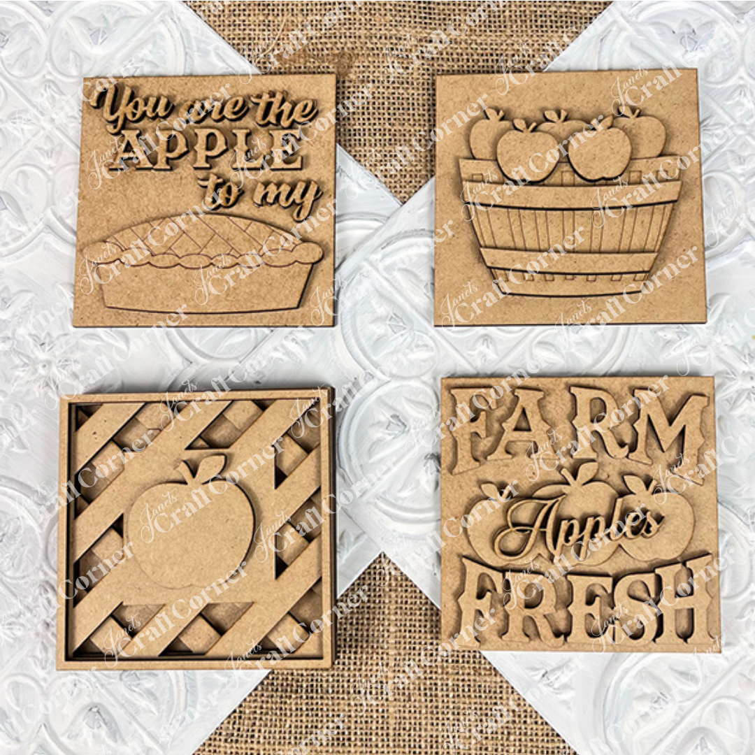 Janet's Craft Corner Apple Swappable Squares DIY kit includes four wooden signs with apple cut-outs: "You are the apple to my pie," a basket, a striped apple, and "Farm Fresh Apples." Perfect for seasonal home decor.