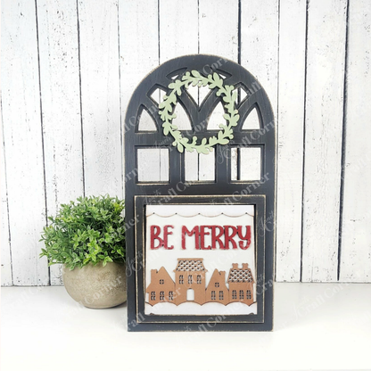 Janet's Craft Corner Arch Window Interchangeable Frame for Squares is a DIY farmhouse decor kit featuring a decorative sign with "BE MERRY," house illustrations, an arch window frame, and a small wreath; perfect for tabletop display.