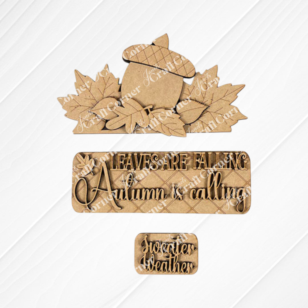 The Autumn Is Calling Interchangeable Insert, a DIY home decor kit from Janet's Craft Corner, showcases hand-painted autumn-themed designs on a textured white and burlap background. The central pieces highlight an acorn surrounded by leaves with the phrase "Leaves are falling, Autumn is calling," accompanied by a smaller piece featuring "Sweater weather." Ideal for interchangeable insert collections or crafting projects.
