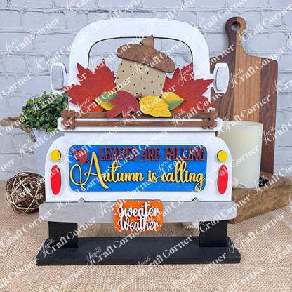 A rustic DIY home decor kit from Janet's Craft Corner features an antique truck base with interchangeable inserts, creatively painted in an autumn theme. The text on the insert says, "Leaves are falling, Autumn is calling, Sweeter weather," and it's charmingly adorned with leaves and an acorn for a seasonal touch.