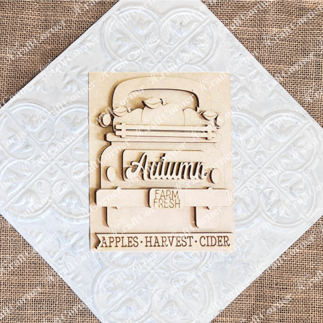 Janet's Craft Corner presents the Autumn Truck Interchangeable Sign, a DIY home decor craft kit featuring a hand-painted wooden plaque. The design includes an intricately carved "Autumn" and a charming truck with "Farm Fresh" on its tailgate, accompanied by the text: "Apples - Harvest - Cider." Ideal for enhancing your seasonal decor.