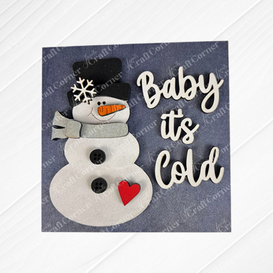 The "Hello Winter Squares" DIY kit by Janet's Craft Corner features a handmade card with a snowman in a black hat, gray scarf, carrot nose, buttons, and red heart. "Baby it's Cold" appears in white—perfect winter decor or tiered tray accent!.