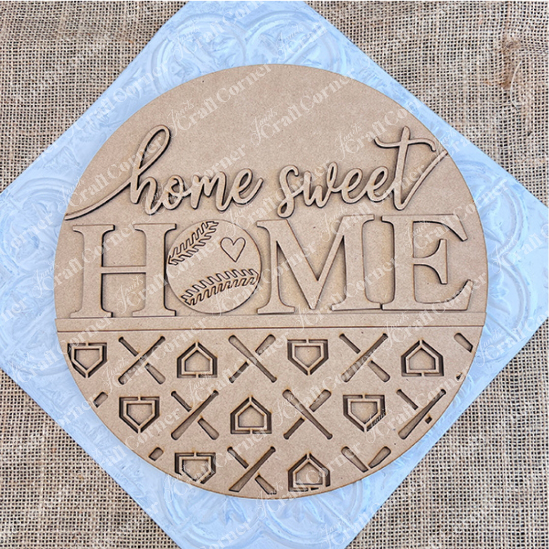 Introducing the "Baseball Home Sweet Home Round" from Janet's Craft Corner. This round wooden DIY sign showcases the phrase "home sweet HOME" along with a baseball door hanger design. The bottom half features intricate cut-out patterns set against a burlap background, and the kit conveniently includes "DIY KIT" labeled in the corner.