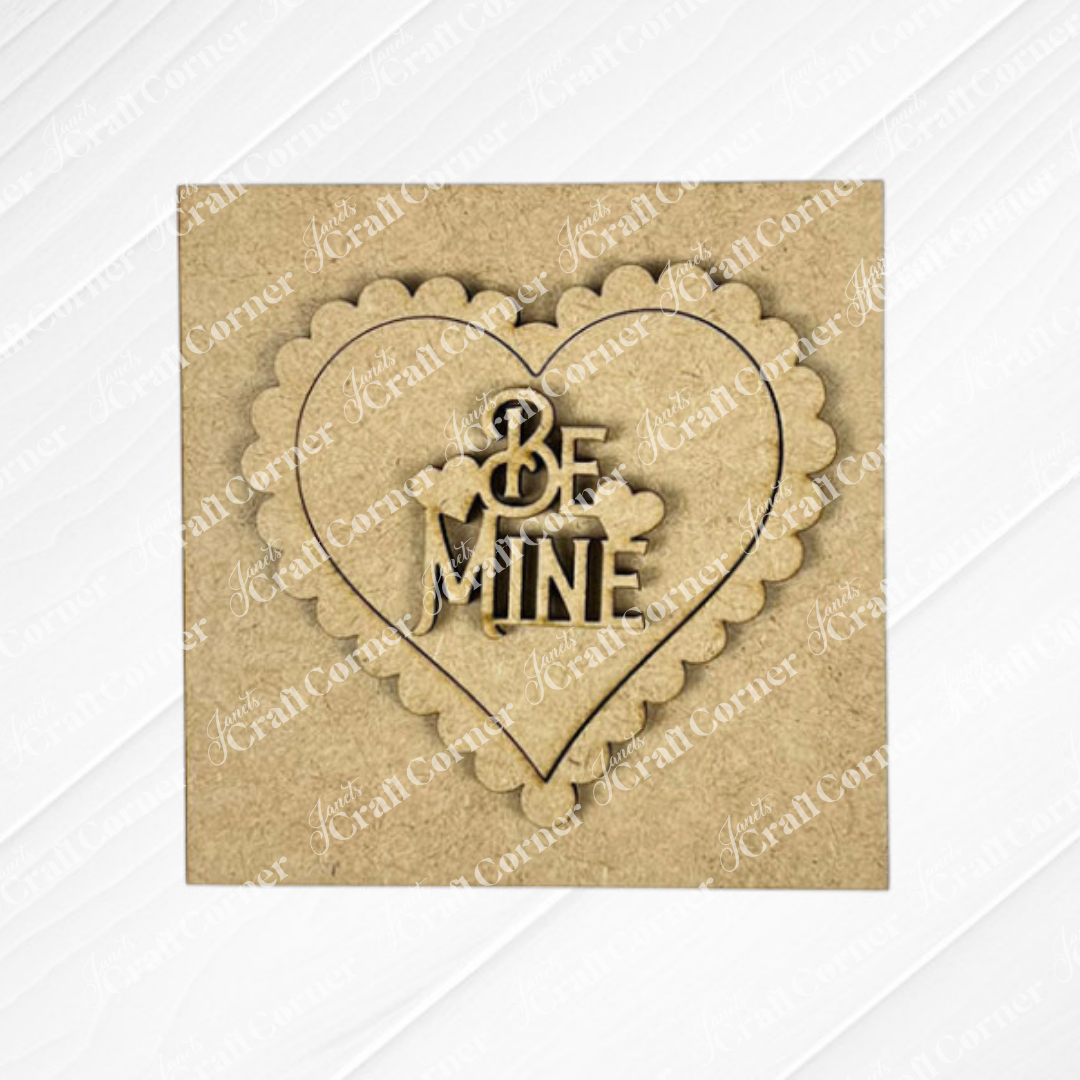 Janet's Craft Corner’s Valentine Squares feature a square brown card with a scalloped heart, smaller inner heart, and "BE MINE" cutout—perfect for DIY seasonal decor or as a charming accent on your tiered tray. Light wood texture background included.