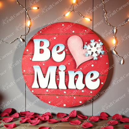 Janet's Craft Corner Be Mine Round Wall Hanger—DIY seasonal home decor craft kit—features "Be Mine" in white, a pink heart, and a snowflake. Hang with string lights above and rose petals below for a festive touch. Set of 1.