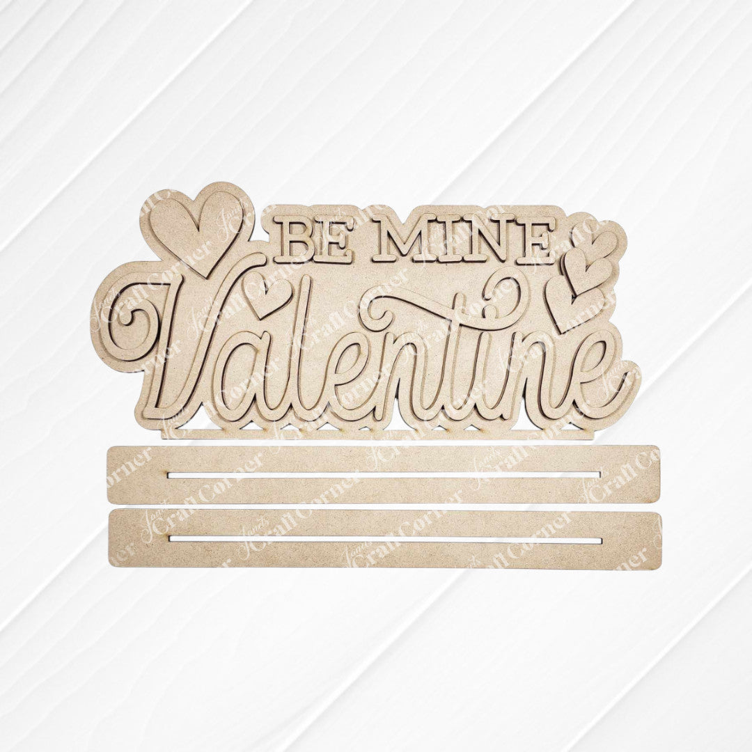 Add charm to your home décor with the "Be Mine Valentine" Word Art from Janet's Craft Corner. This hand-painted wooden cutout sign features cursive text and heart shapes on a white background, complete with two horizontal slots for DIY projects.