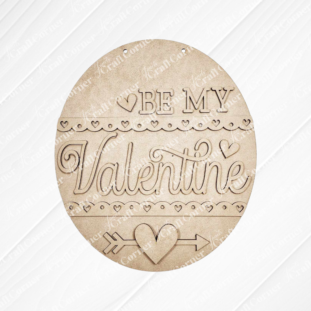 Janet's Craft Corner presents the "Be My Valentine Door Hanger," a chic DIY home decor kit featuring a round, wooden design with hearts, an arrow, and elegant engraving on a white wood-paneled background.
