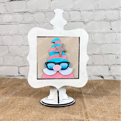 The Summer Lovin Swappable Squares DIY craft kit from Janet's Craft Corner features a colorful gnome with sunglasses, pink hat, and silver star on a white decorative frame—ideal for tiered tray decor or pairing with wood cut-outs.