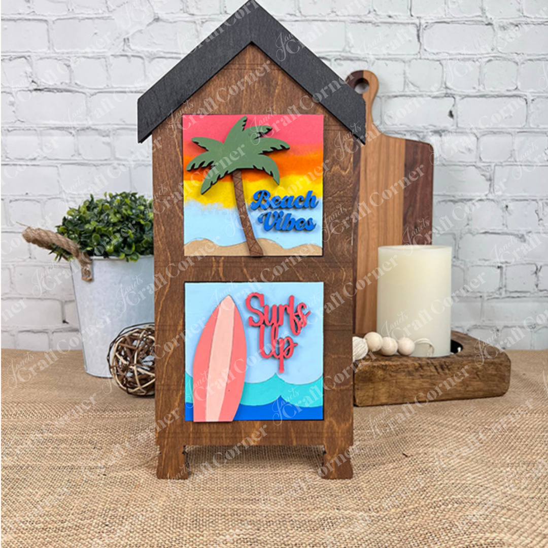 The Summer Beach Squares DIY craft kit by Janet's Craft Corner features wooden house-shaped stands with colorful palm tree and surfboard cut-outs, perfect as tiered tray signs to brighten your coffee bar or seasonal home decor.