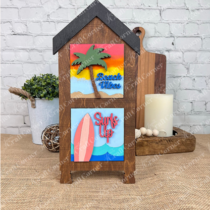 The Summer Beach Squares DIY craft kit by Janet's Craft Corner features wooden house-shaped stands with colorful palm tree and surfboard cut-outs, perfect as tiered tray signs to brighten your coffee bar or seasonal home decor.