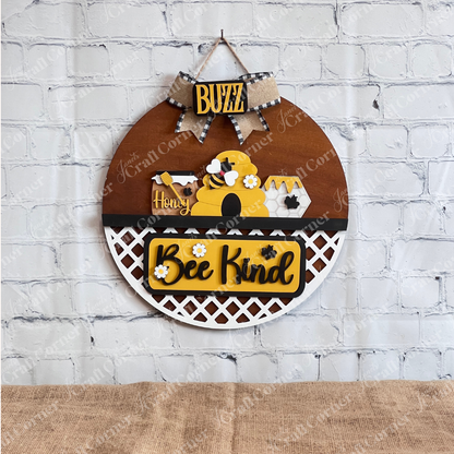 Discover the Bee Interchangeable Insert - Painted from Janet's Craft Corner. This round wooden decorative hanging sign features a charming beehive, bees, and honeycomb motif. It includes the words "Buzz," "Honey," and "Bee Kind" with a white lattice pattern at the bottom, offering versatile decor options with its interchangeable bee inserts.