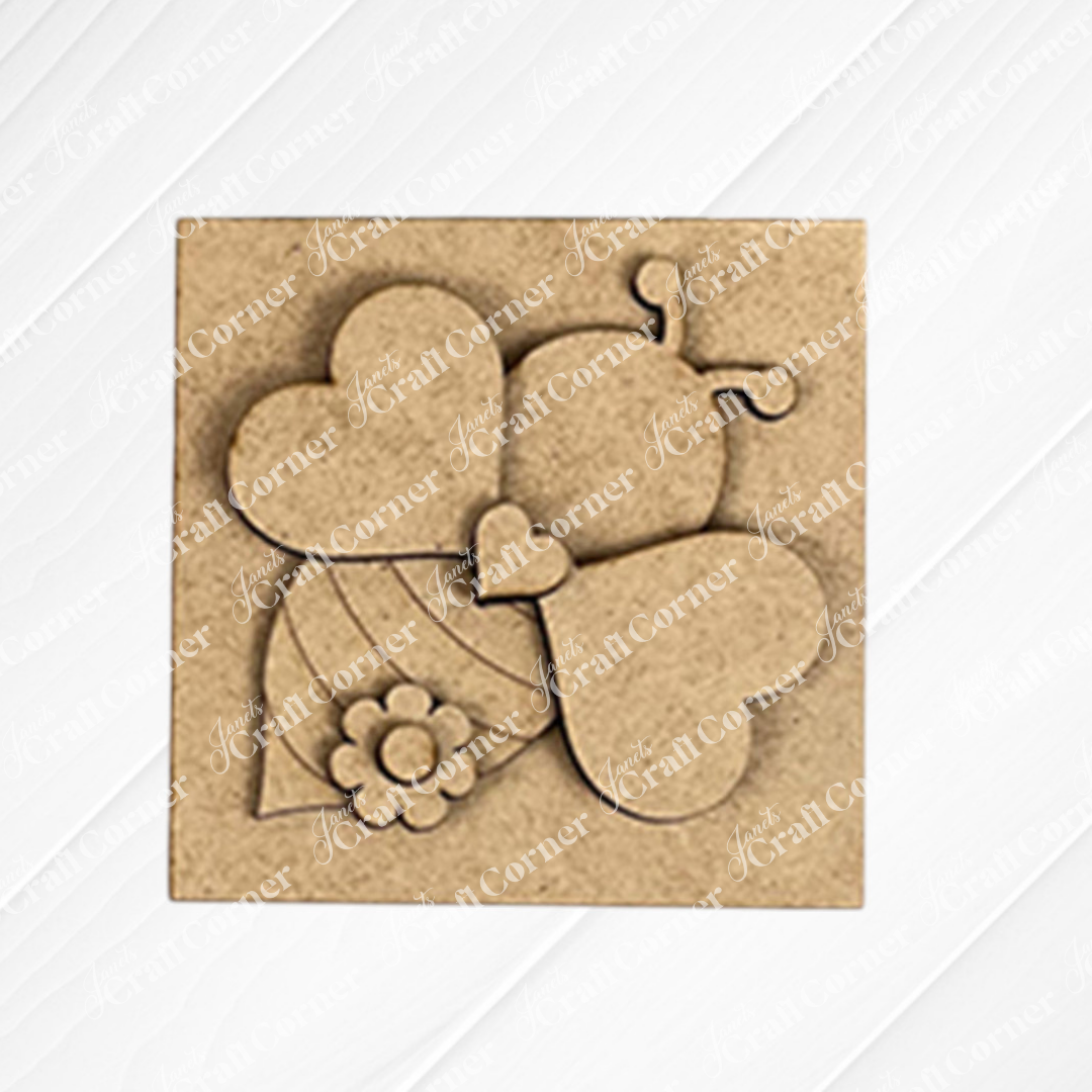 The Bee Swappable Squares by Janet's Craft Corner features a heart-winged, striped bee with a flower accent, adding handmade charm as delightful home decor on a textured white surface.