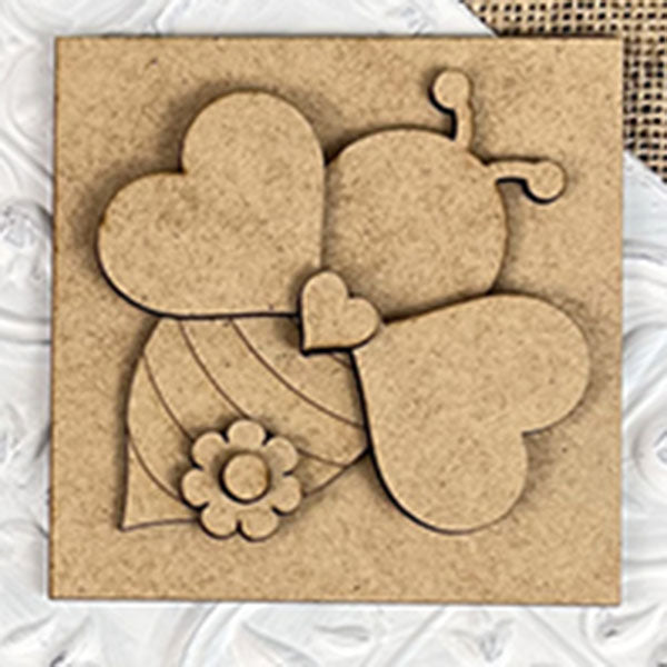 The Bee Swappable Squares by Janet's Craft Corner features a heart-winged, striped bee with a flower accent, adding handmade charm as delightful home decor on a textured white surface.