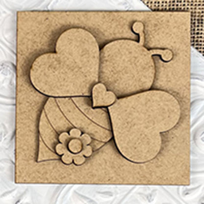 The Bee Swappable Squares by Janet's Craft Corner features a heart-winged, striped bee with a flower accent, adding handmade charm as delightful home decor on a textured white surface.