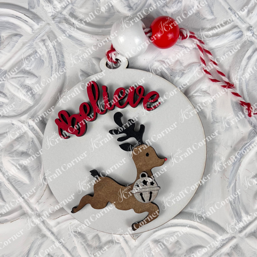 The Round Christmas Ornaments from Janet's Craft Corner feature a cutout of a leaping reindeer in a festive sweater, with the word "Believe" elegantly displayed in red above. Adorned with beads and a red-and-white cord, this intricate decoration adds joy and charm to any DIY Decoration Kit collection.