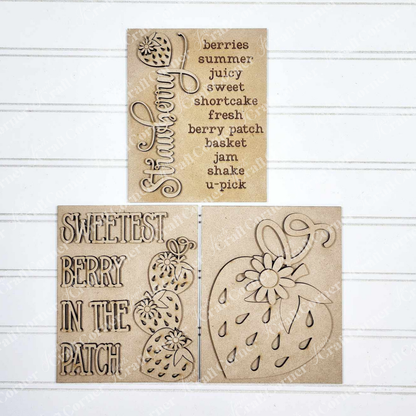 Displayed against a white plank wall, signs from Janet's Craft Corner, this set of Berry Sweet Switchable Farmhouse Signs are DIY seasonal home decor kits with a strawberry theme. One features the word Strawberry with a berry and words that evoke a trip to the berry patch, another features a large strawberry and one that features the words “Sweetest Berry in the Patch” and a stack of 3 berries completes these cozy signs.