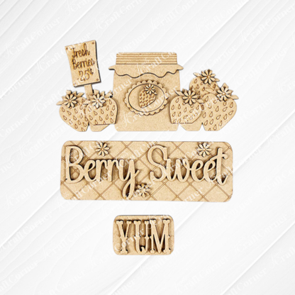 Arranged on a white textured background are wooden cutouts from Janet's Craft Corner, featuring a "Fresh Berries - 25¢" sign, a jam jar, strawberries, "Berry Sweet" text, and a "YUM" piece. This Berry Sweet Interchangeable Insert is part of their DIY home decor kit that's perfect for customizable farmhouse décor on a charming burlap surface.