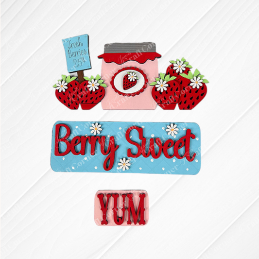 Decorative cookies shaped like strawberries, a jam jar, and charming text are beautifully displayed on a white patterned surface. This delightful kit from Janet's Craft Corner includes messages like "Berry Sweet" on a blue background, "Fresh Berries 25¢" on a small sign, and "YUM" in red—an ideal way to infuse farmhouse charm into your Berry Sweet Interchangeable Insert collection.
