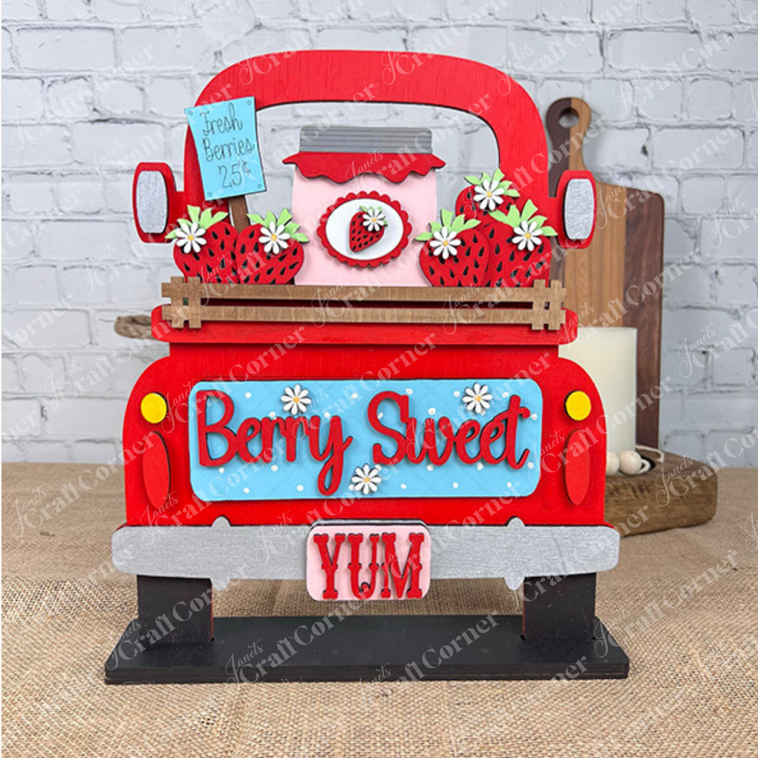 The Berry Sweet Interchangeable Insert from Janet's Craft Corner is a charming DIY home decor kit perfect for farmhouse décor. It features a decorative wooden sign with a red truck carrying strawberries and a jar, labeled "Fresh Berries 25¢," surrounded by daisies and set against a brick wall backdrop. The display also reads "Berry Sweet YUM," making it ideal for adding an interchangeable touch to your home décor.