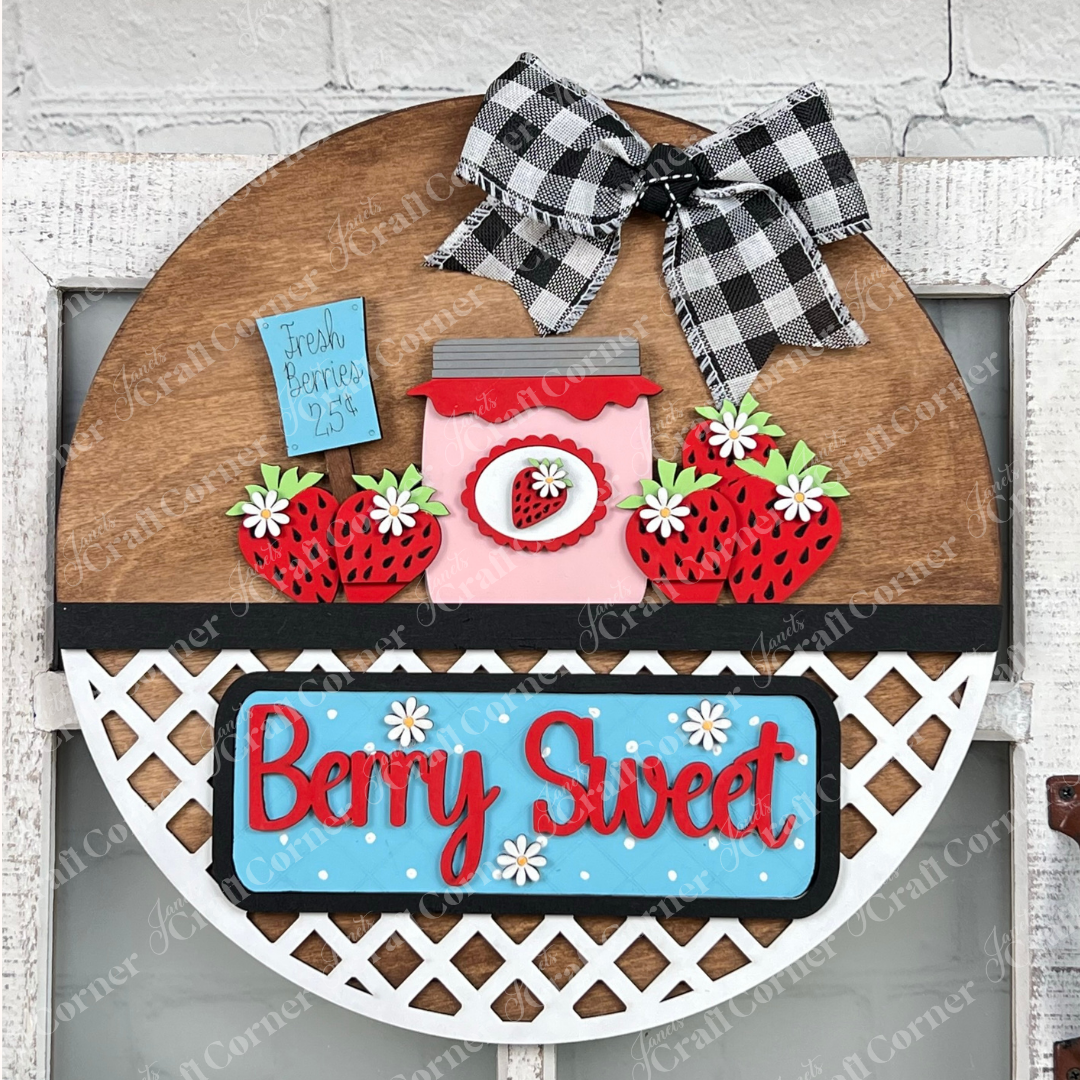 Introducing the "Berry Sweet Interchangeable Insert" from Janet's Craft Corner, a delightful DIY home decor kit. This charming farmhouse piece combines strawberries, a heart-shaped jar, and a "Fresh Berries 25¢" label. The phrase "Berry Sweet" stands out in red on blue with white daisies, complemented by a black and white checkered bow at the top.