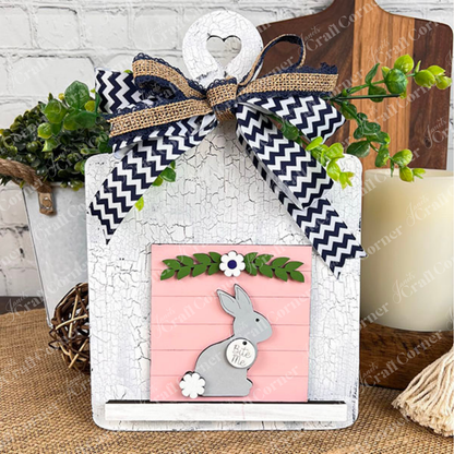 Janet's Craft Corner’s Easter Bunny Squares show a gray bunny and "Bunny Kisses" on pink with green leaves and white flowers, perfect tiered tray decor, finished with a chevron ribbon, burlap bow, and greenery.