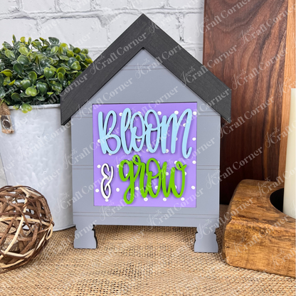 Decorate your space with Janet's Craft Corner "Bloom & Grow Squares," a house-shaped sign with a swappable purple panel and white-green lettering—perfect for tiered trays, plant displays, or as accent decor.