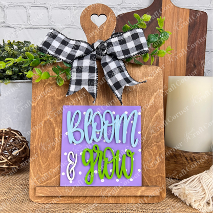 Janet's Craft Corner's Bloom & Grow Squares features a heart-cutout wooden board with a plaid bow and a purple sign reading "BLOOM & GROW" with green accents—ideal as tiered tray decor for any textured surface.