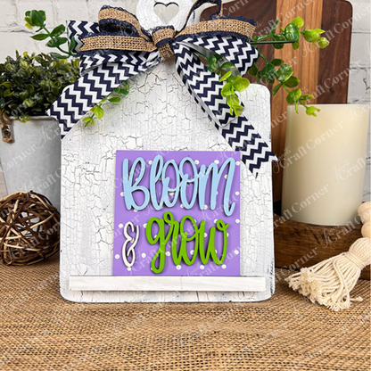 Janet's Craft Corner's Bloom & Grow Squares is a decorative white sign with a black and white chevron bow and greenery, featuring playful “Bloom & Grow” lettering—perfect for tiered trays or rustic wooden table displays.