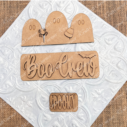 Featuring the "Boo Crew Interchangeable Insert" DIY home decor kit from Janet's Craft Corner, this hand-painted craft set includes wooden ghost shapes, a spider, and a candy corn on a textured background. It also showcases the phrases "Boo Crew" with a bat and "Spooky," making it an ideal interchangeable accessory for adding festive charm to any space.