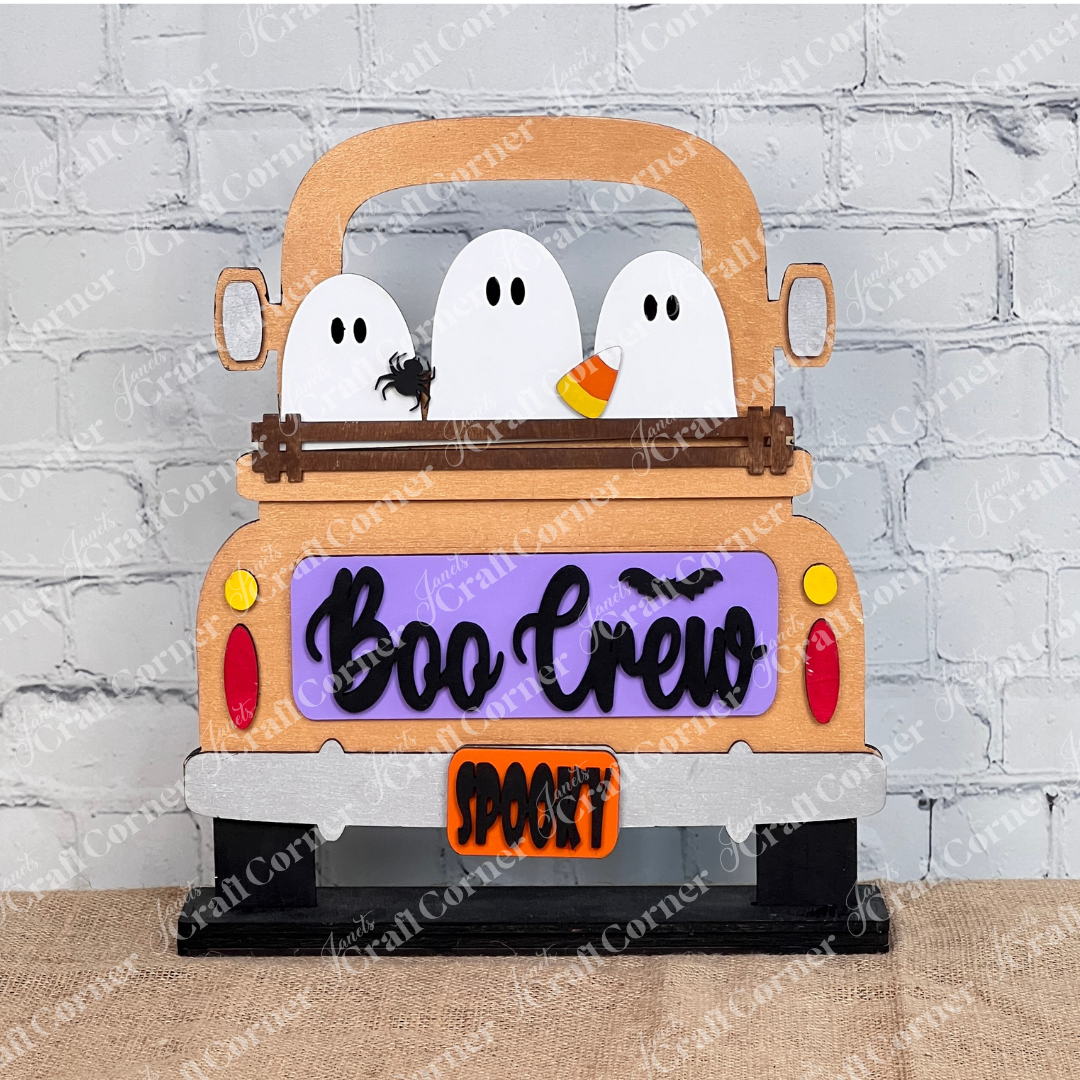 Janet's Craft Corner offers the Boo Crew Interchangeable Insert, a home decor set featuring three cartoon ghosts in a colorful pickup with charming sidekicks—a bat and spider—all set against a white brick wall.