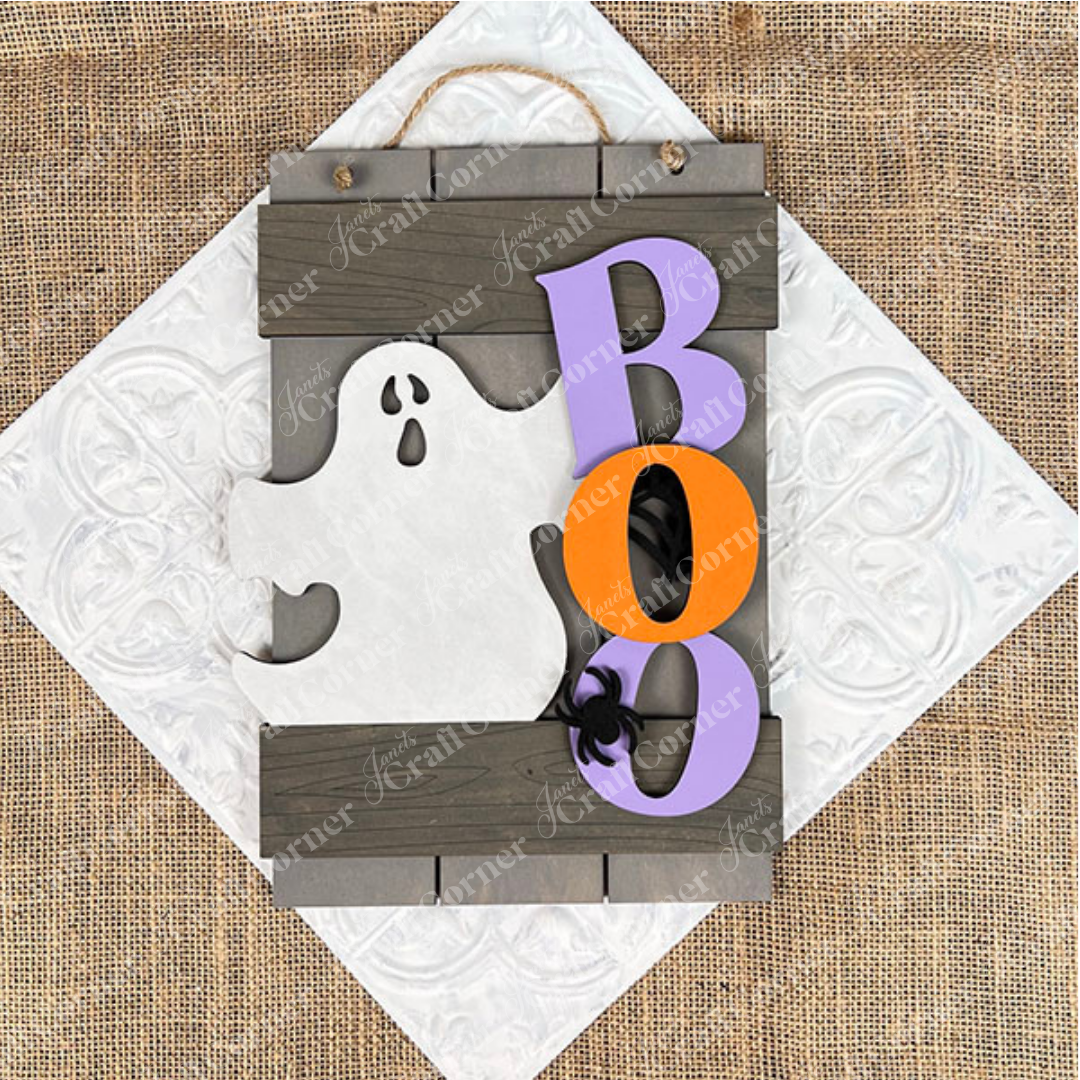 The Boo Fence Door Hanger from Janet's Craft Corner is a versatile DIY kit. It showcases a wooden white ghost silhouette next to vibrant "B," "O," and "O" letters in purple and orange. Ideal for your door, it enhances your home décor with its festive touch and burlap-textured background.