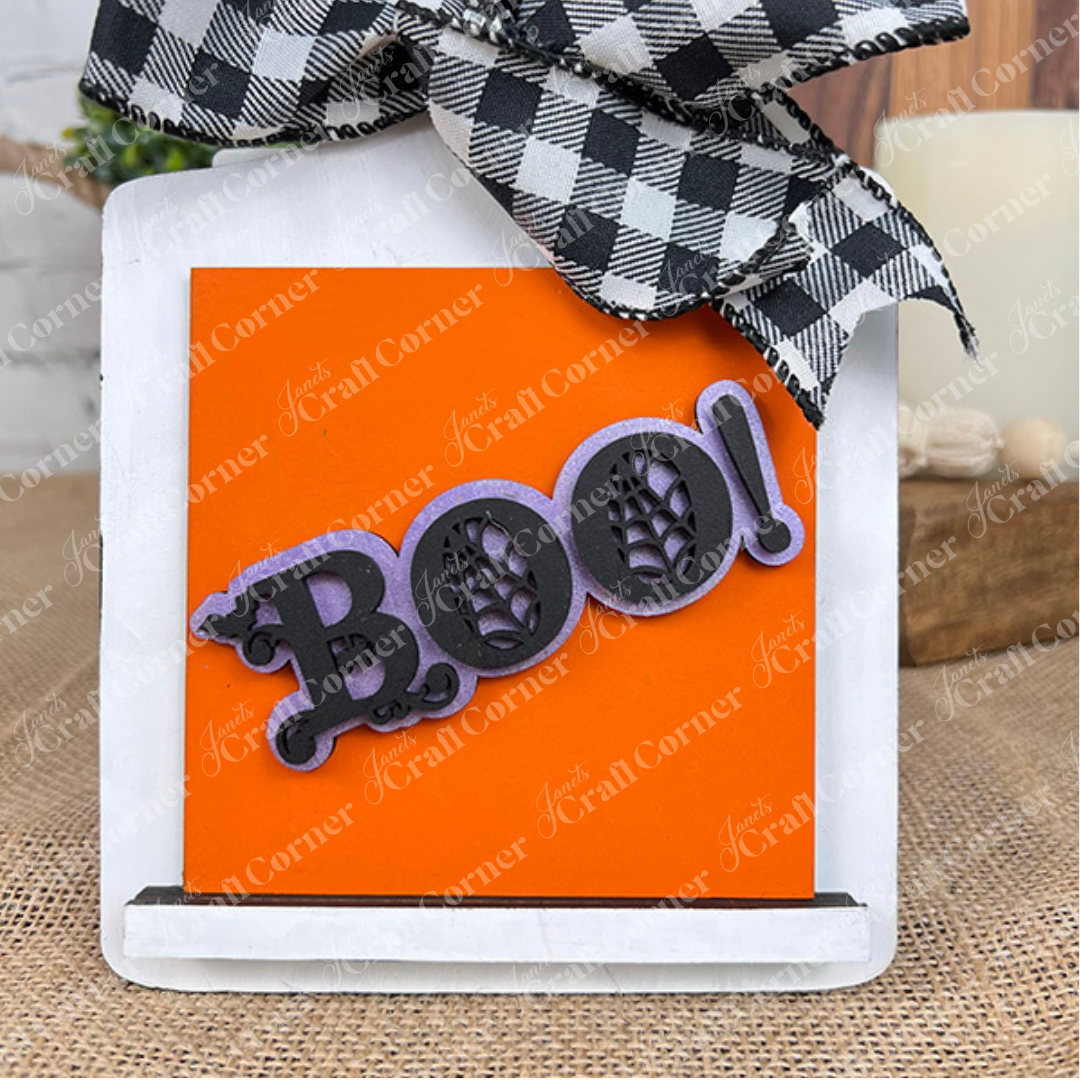 Janet's Craft Corner's Halloween Squares features wood cut-outs, a black and white checkered bow, and an orange "Boo!" sign with spider web details—perfect for tiered tray decor.