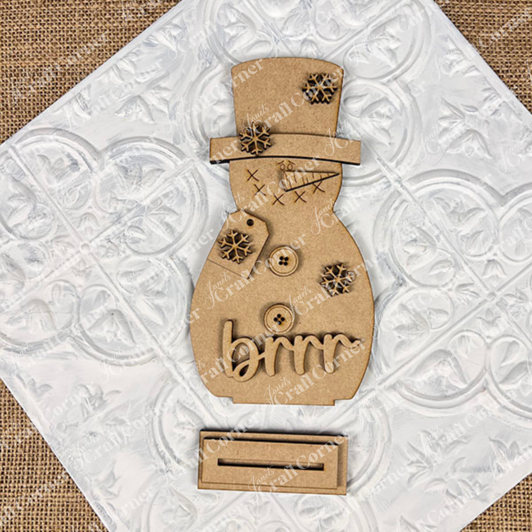 Add festive charm to your home with Janet's Craft Corner Snowman Shelf Sitters—featuring buttons, snowflakes, stitched details, and "brrr" text on a white tile with a separate base.