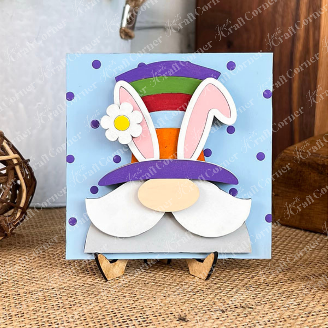 A whimsical bunny with a large hat, pink ears, white beard, and flower sits on blue with purple polka dots—perfect for Hello Easter Squares by Janet's Craft Corner, a DIY kit with wood cut-outs and stand.