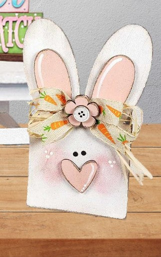 Add charming farmhouse accents to your space with the Easter Bunny Decor Set - Painted by Janet’s Craft Corner, featuring a wooden bunny with a heart-shaped nose, blushing cheeks, and a bow adorned with flower and carrot designs. Carefully crafted from painted wood, this delightful piece is perfect for adding whimsical style to your home decor.