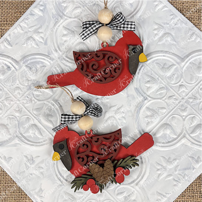 The Cardinal Ornament from Janet's Craft Corner showcases detailed red cardinal designs with intricate patterns and black-and-white checkered bows. Ideal for holiday décor, these ornaments are enhanced by elegantly strung wooden beads set against a textured white background.