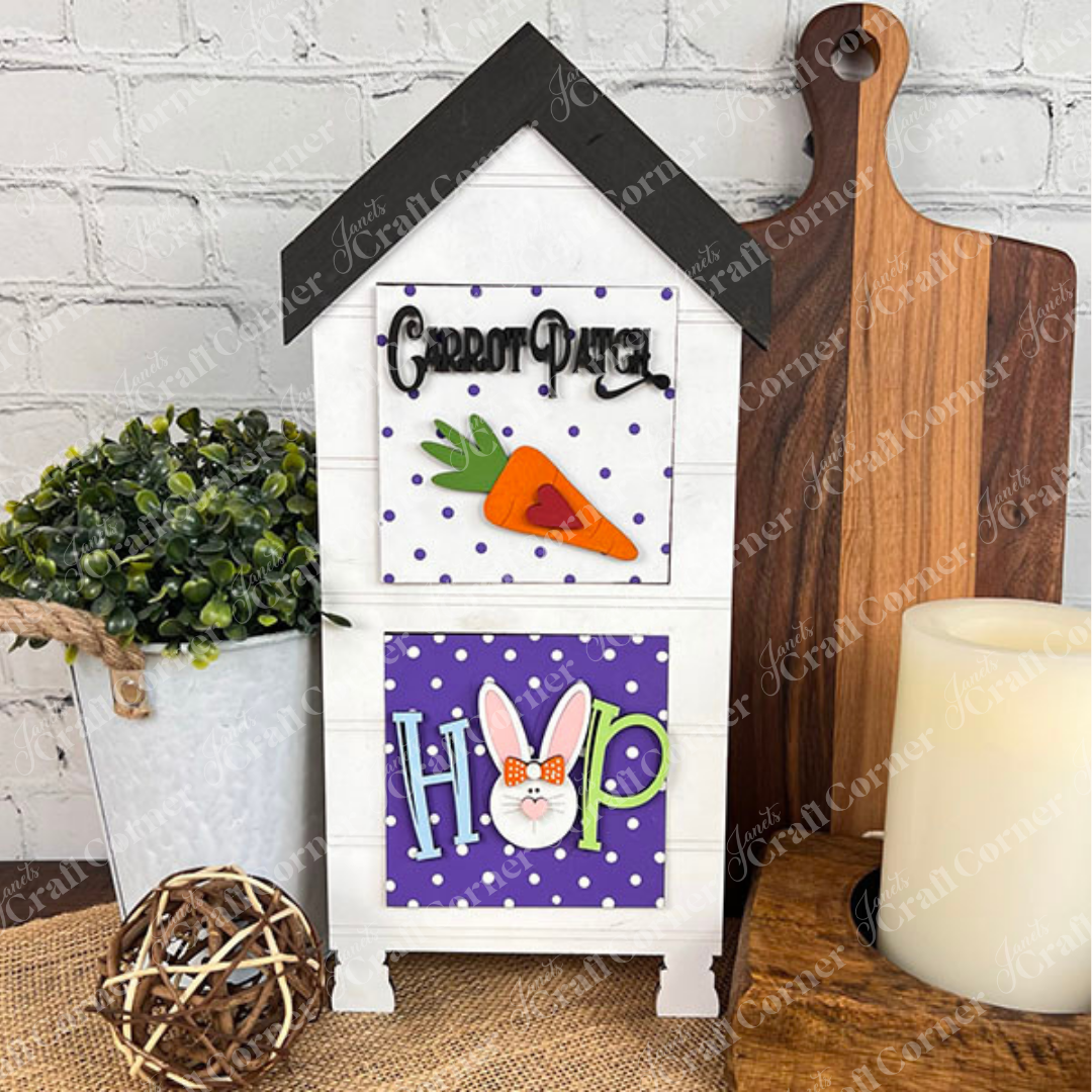 Janet's Craft Corner Easter Bunny Squares is a decorative house-shaped shelf with wood cut-outs: one panel shows a carrot and "Carrot Patch," another has "HOP" with a bunny face. Perfect for tiered tray decor, styled with seasonal accents.